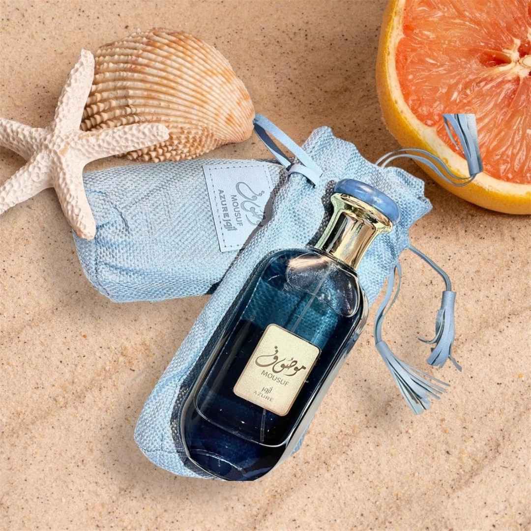 Ard Al Zaafaran Mousuf Azure Unisex EDP 100ml bottle and pouch on beach sand with seashells and fruit