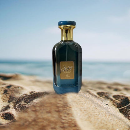 Ard Al Zaafaran Mousuf Azure Unisex EDP 100ml bottle standing on beach with sea in background