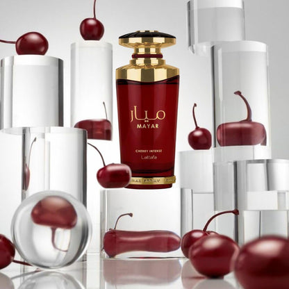 Red perfume bottle with gold cap labeled 'MAYAR' surrounded by cherries on a reflective surface.