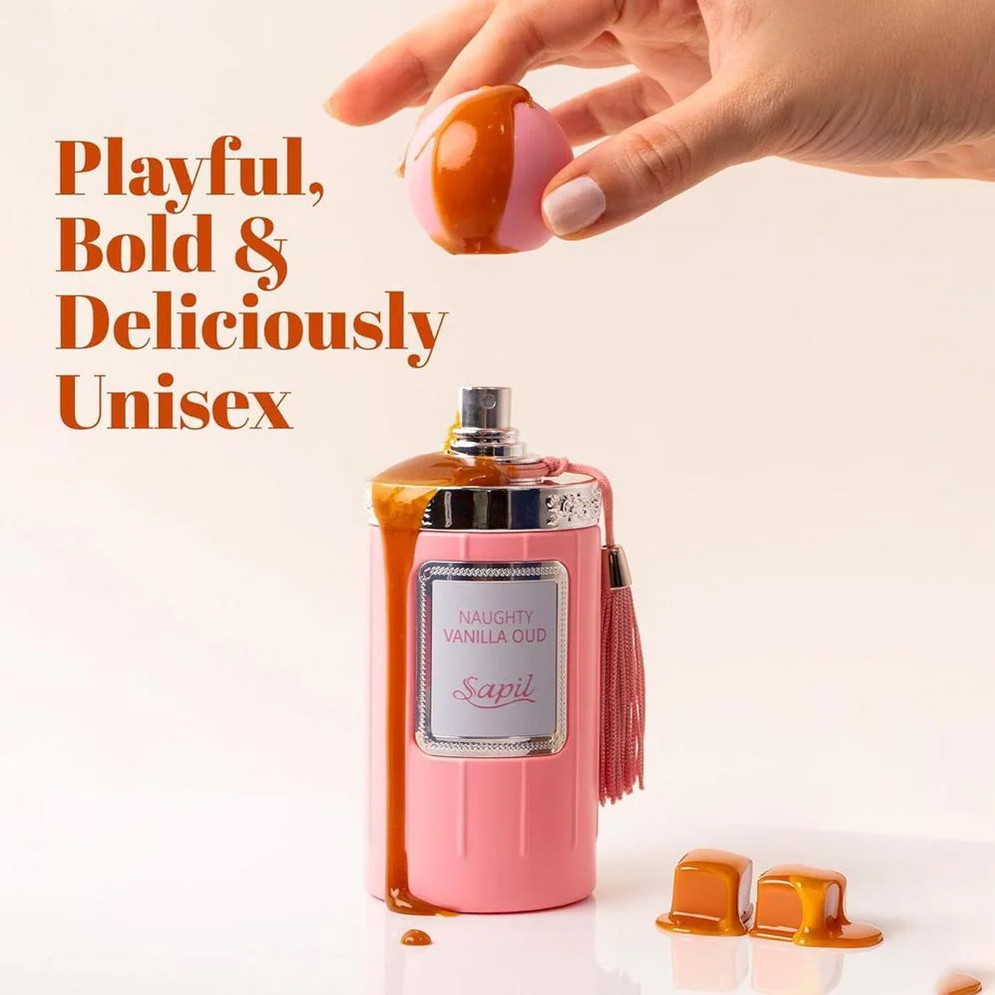 Sapil Naughty Vanilla Oud Unisex EDP 100ml  Pink perfume bottle with tassel and orange cap, hand holding cap, text 'Playful, Bold & Deliciously Unisex'.