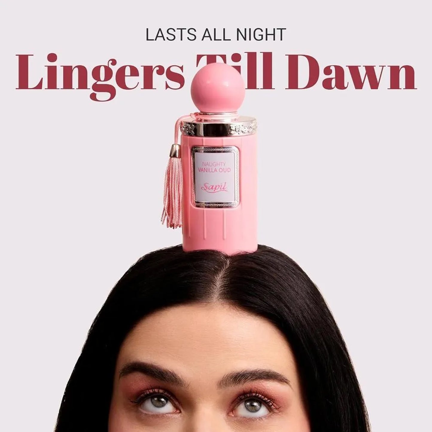 Sapil Naughty Vanilla Oud Unisex EDP 100ml Pink perfume bottle on a woman's head with text 'Lasts All Night Lingers Till Dawn' on a light pink background