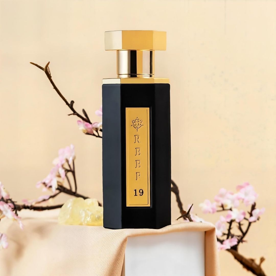 Reef 19 luxury perfume bottle with black and gold design displayed with jasmine blossoms and white musk resin, highlighting elegant floral Arabian fragrance notes.