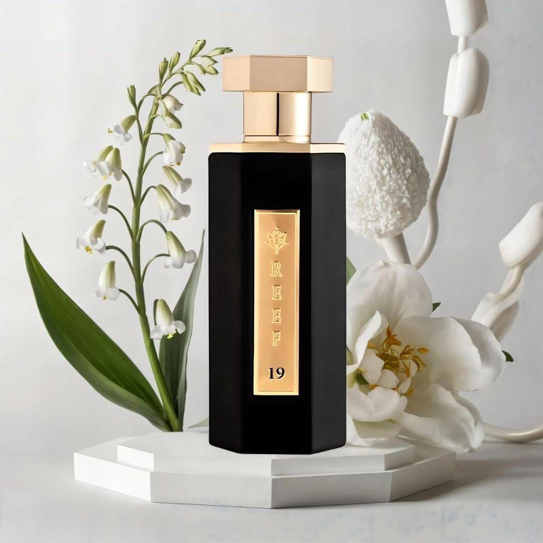 Reef 19 luxury perfume bottle with gold cap and black design displayed with lily of the valley and white floral notes representing elegant Arabian fragrance ingredients.