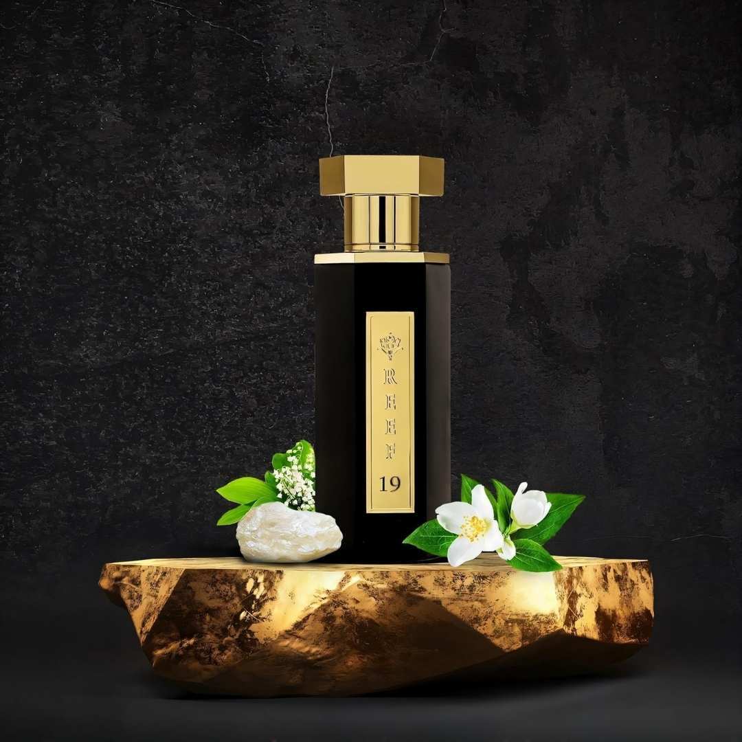 Reef 19 luxury perfume bottle with gold cap displayed on stone base with white musk resin, jasmine flower, and lily of the valley representing elegant floral fragrance notes.