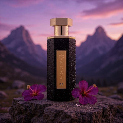 Reef 33 luxury black and gold perfume bottle displayed on a rock with purple flowers against a dramatic mountain sunset landscape, representing an elegant woody floral fragrance.