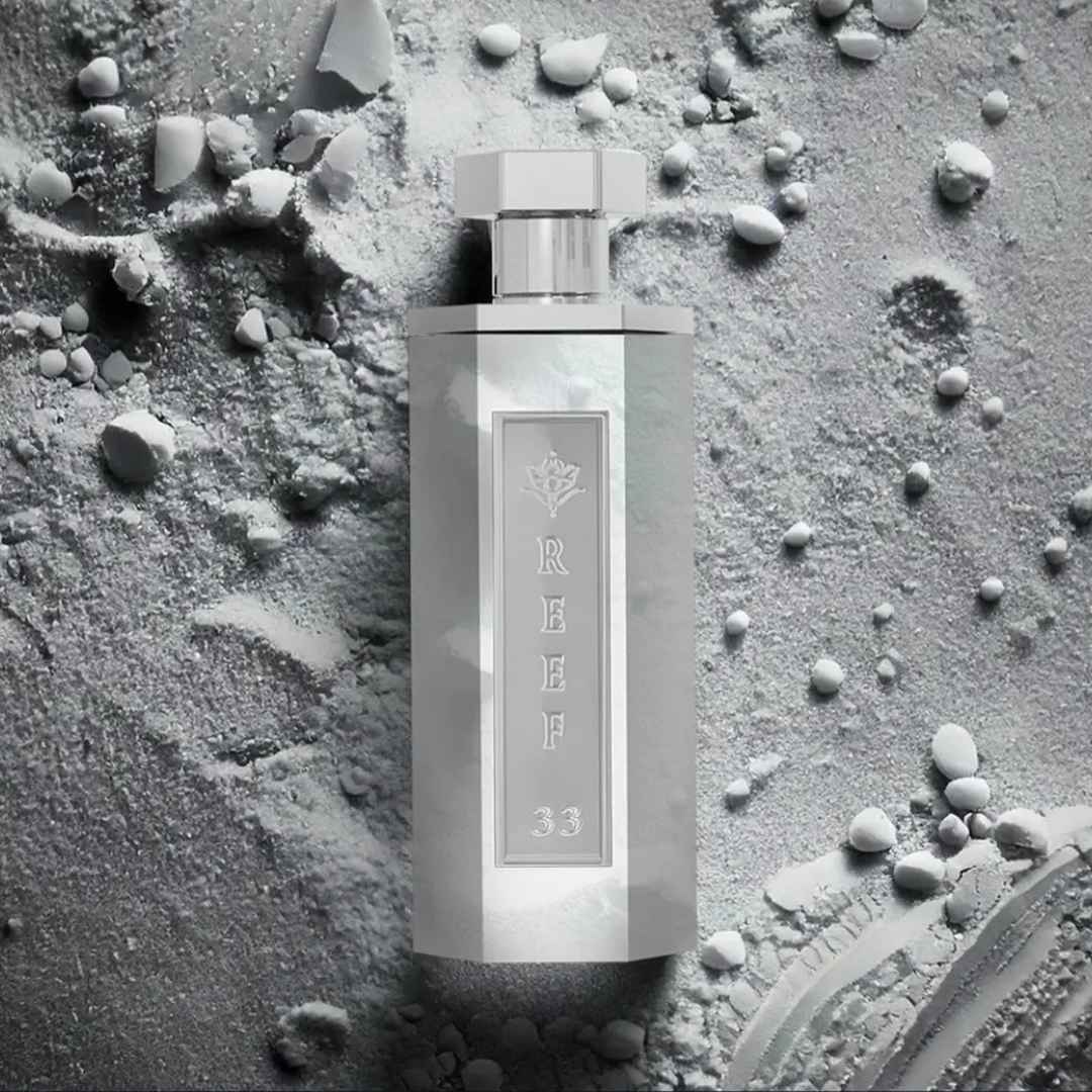 Reef 33 luxury white perfume bottle displayed on textured powder surface highlighting a clean, soft, and elegant fragrance concept.